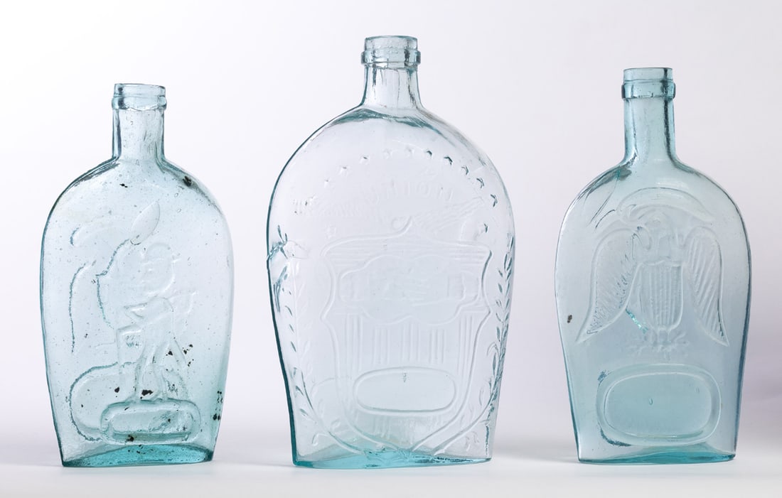 THREE HISTORICAL GLASS FLASKS: Mid-19th century. All aqua, includes a Union/Clasped Hands, 8.5" high; together with a Cunningham, Pittsburgh, Pennsylvania eagle, 8" high; and a eagle/Pike's Peak, 7.75" high. Provenance: the collect