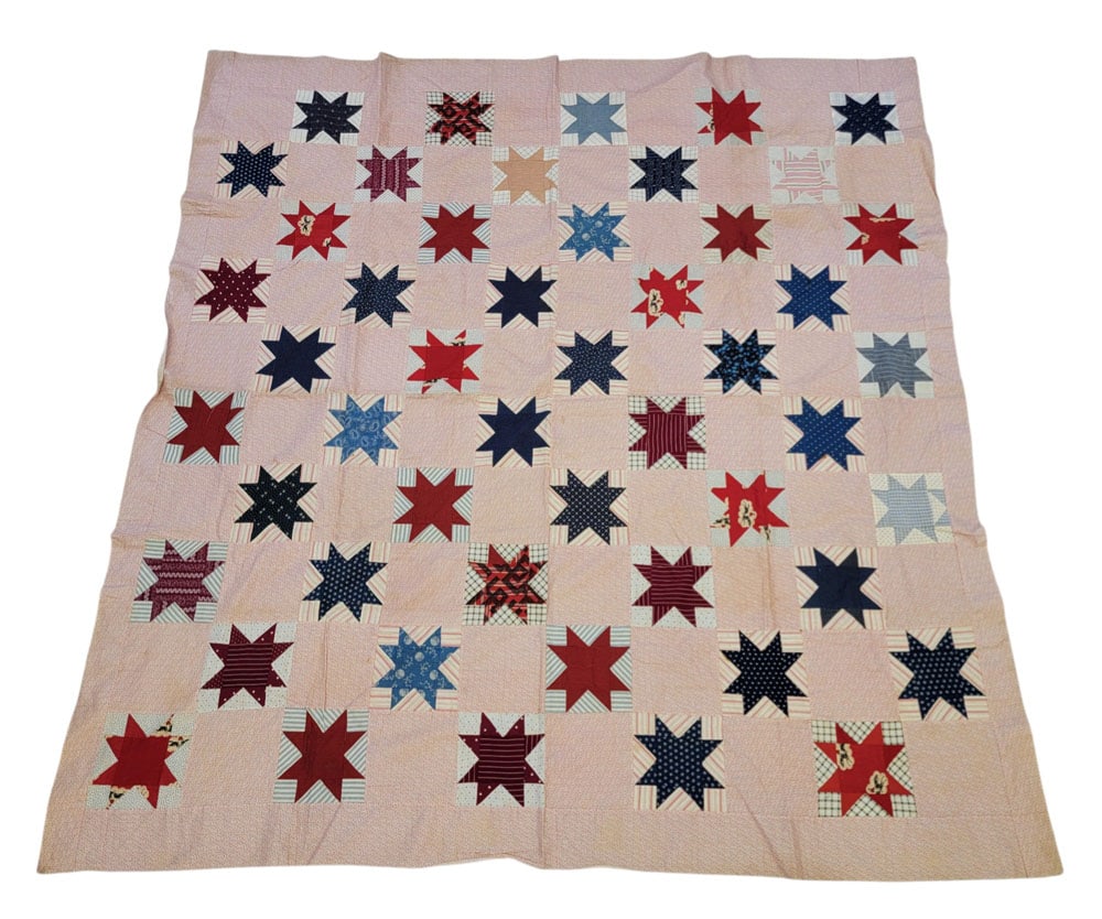 OHIO STAR QUILT TOP: American, 19th century, cotton. A quilt top with alternating blocks of printed pink fabric and pieced blocks of printed fabrics, mostly in blues and reds, in an Ohio Star pattern, with a pink rectangu