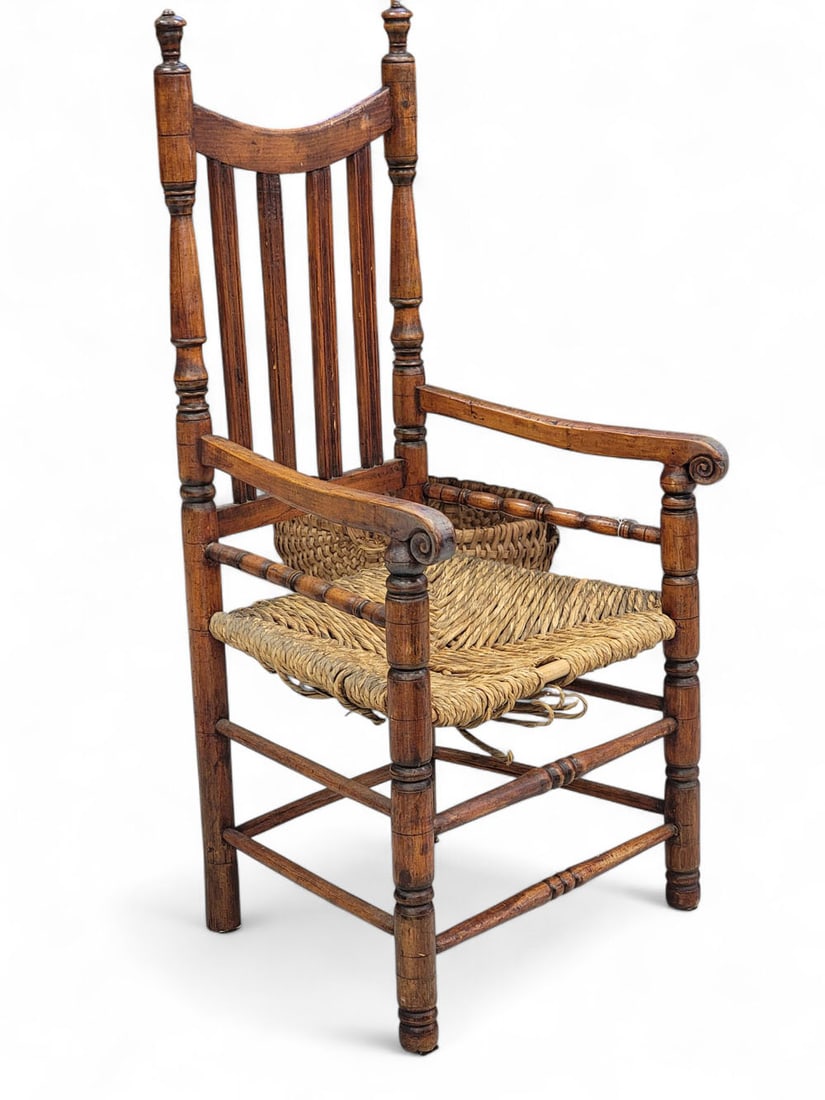 BANNISTER-BACK ARMCHAIR: New England, 18th century, mixed woods. Sausage-turned split bannister chair. Bowed crest rail over four reeded bannister splats, with sausage-turned posts and legs, scrolled arms, rush seat, seven tu