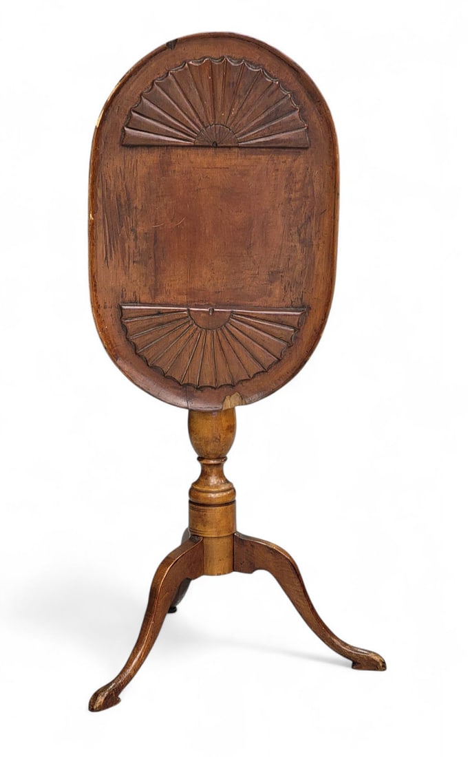 COLONIAL REVIVAL CANDLESTAND: Michigan, early 20th century, cherry. Tilt-top stand, the top carved with two large fans at either end. Turned pedestal over three arch-carved legs. 25" high, 20.75" wide, 13.5" deep. Provenance: from