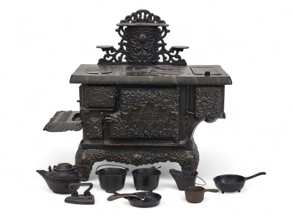 "TRIUMPH" TOY STOVE: Kenton Hardware, Kenton, Ohio, late 19th century, cast iron. Elaborate toy stove with many pots, pans, and kettles. 14" high. Provenance: an Ohio collection. Affordable, in-house shipping is available