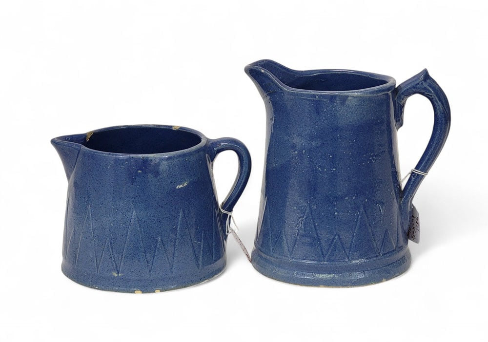 TWO MOLDED BLUE RUCKEL'S POTTERY PITCHERS: American, early 20th century, stoneware. Two solid-blue, molded pitchers by Ruckel's Pottery (unmarked). Same design of "pine forest"-like triangles along the bottom, in a tall and a short form. 8.25"