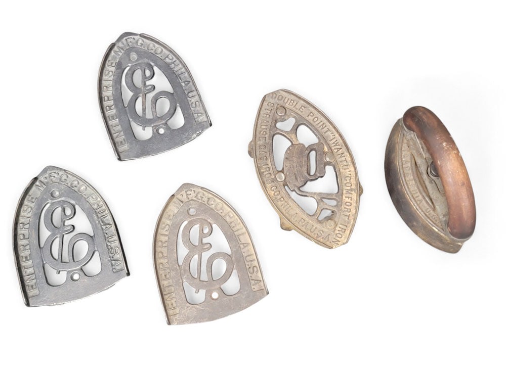 COLLECTION OF PHILADELPHIA-MADE TRIVETS AND IRON: Late 19th-early 20th century, cast iron. Three identical trivets by the Enterprise Manufacturing Corp, Philadelphia (1" high, 4.5" wide, 6" long), plus one Mary Potts Sad Iron by same Corp (5" high, 4