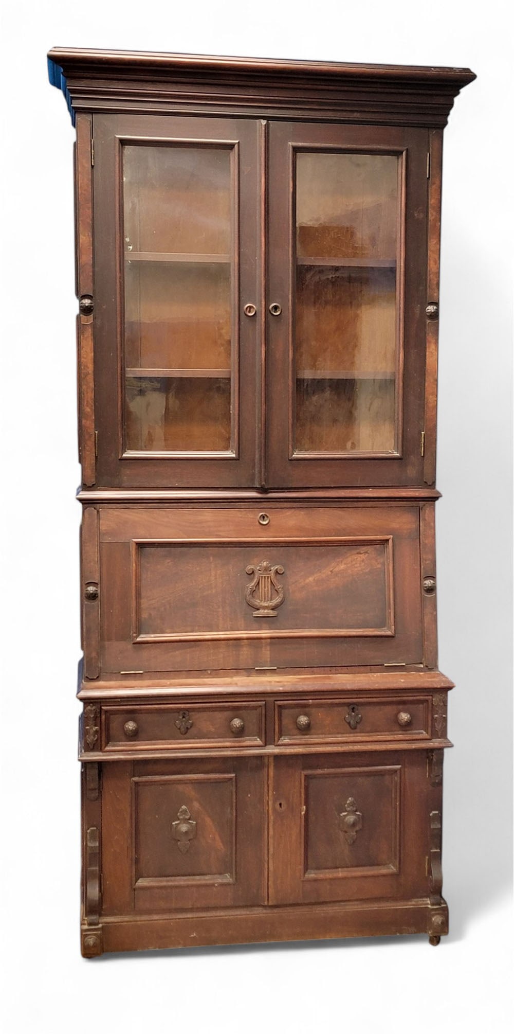 VICTORIAN DESK-AND-BOOKCASE: American, late 19th century. Walnut. Upper case has prominent cornice over two glazed doors with two shelves within. Lower case has slant-top desk with carved lyre applied to front, over two drawers,