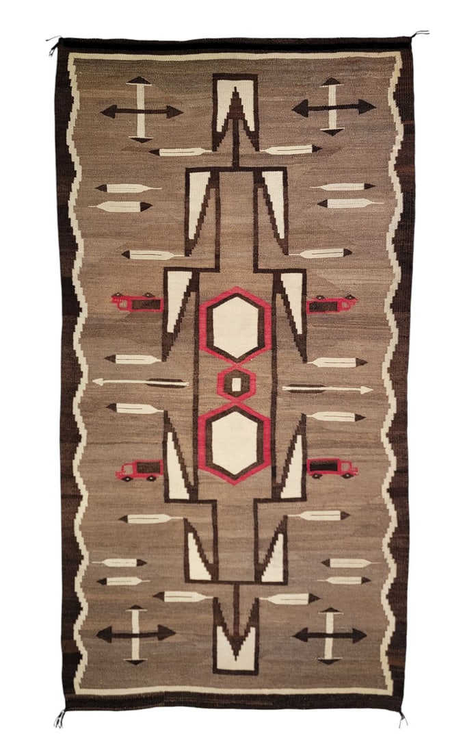 NAVAJO WEAVING WITH TRUCK DESIGN: Southwestern United States, c. 1920-1940, wool. Navajo Crystal-style rug featuring trucks, feathers, arrows, and wing-like triangles, with wavy border and tied corners. Shades of brown, red, and cream