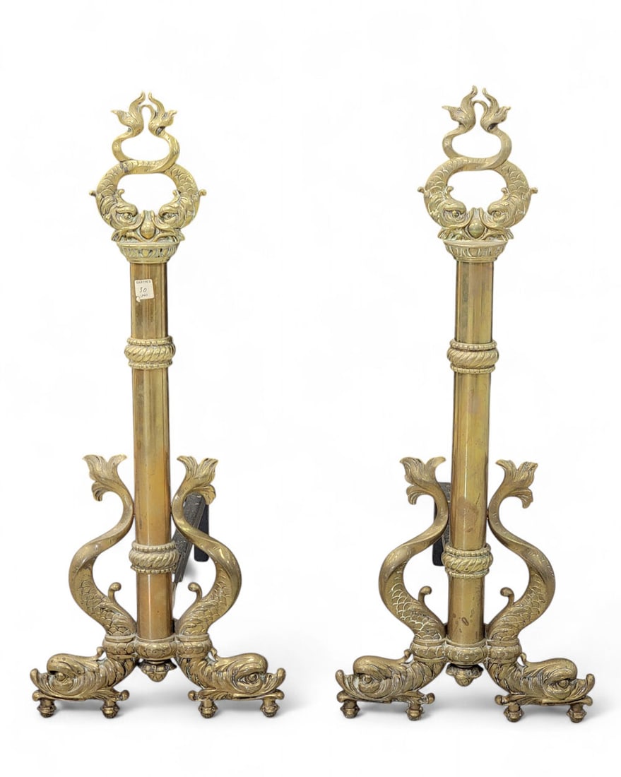 PAIR OF ROCOCO-STYLE BRASS ANDIRONS: Late 19th-early 20th century. Central rod with ropelike bands, pair of dolphins at top with crossed tails making two rings. Dolpins at bottom curve into legs, with ball feet below. Both bearing former
