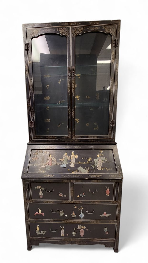 CHINOISERIE DESK-AND-BOOKCASE: 20th century. Black-lacquered body, gold-painted designs along borders and edges. Panels of sides, drawers, and desk top accentuated with applied carved stone figures: flowers, leaves, birds, women, a