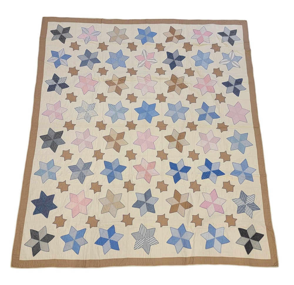 SIX POINTED STAR APPLIQUE QUILT: American, 20th century, cotton. A six-pointed star quilt composed of large six-diamond stars with printed blue, brown, pink, and grey fabrics, offset with smaller free-hand six-pointed stars in solid