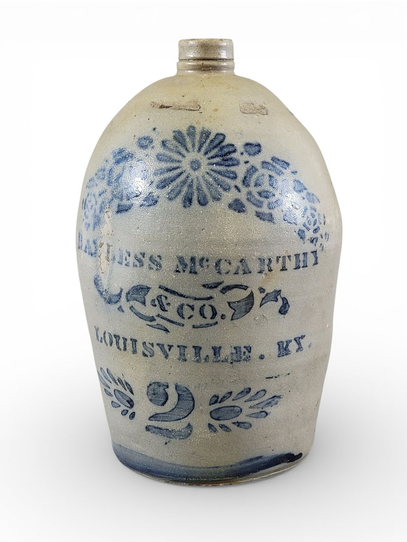DECORATED KENTUCKY STONEWARE JUG: Southwestern Pennsylvania, c. 1875, retailed by Bayless, McCarthey & Co., Louisville. Two-gallon jug with cobalt stenciled decoration, including flowers, 14" high. Provenance: the collection of the la