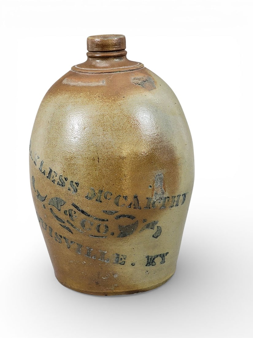 KENTUCKY STONEWARE JUG: Southwestern Pennsylvania, c. 1875, retailed by Bayless, McCarthey & Co., Louisville. One-gallon jug with cobalt stenciled decoration. 11" high. Provenance: the collection of the late Dr. Jerry Phelps