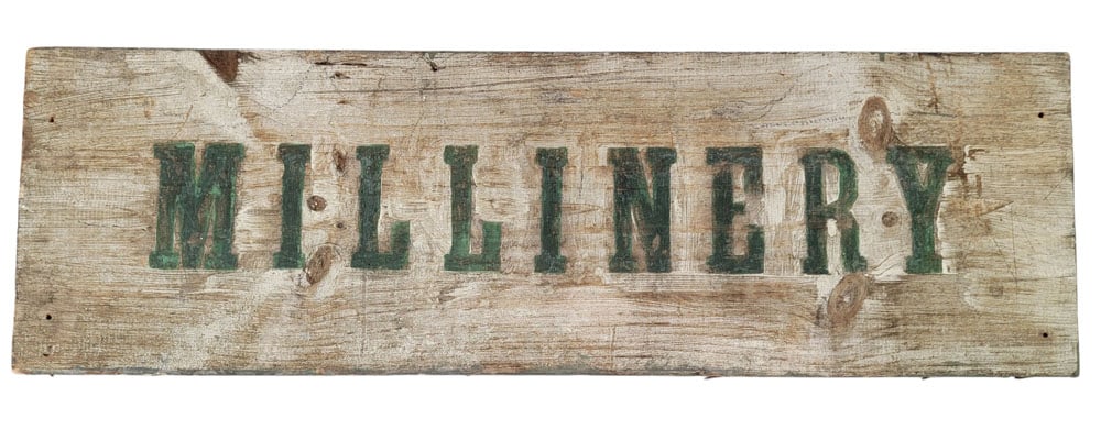 MILLINERY TRADE SIGN: American, 19th century, painted pine. A Millinery advertising trade sign, plank painted white with green stenciled lettering. 10.75" high, 34.25" wide. 1.25" thick. Provenance: an Ohio collection. NOT