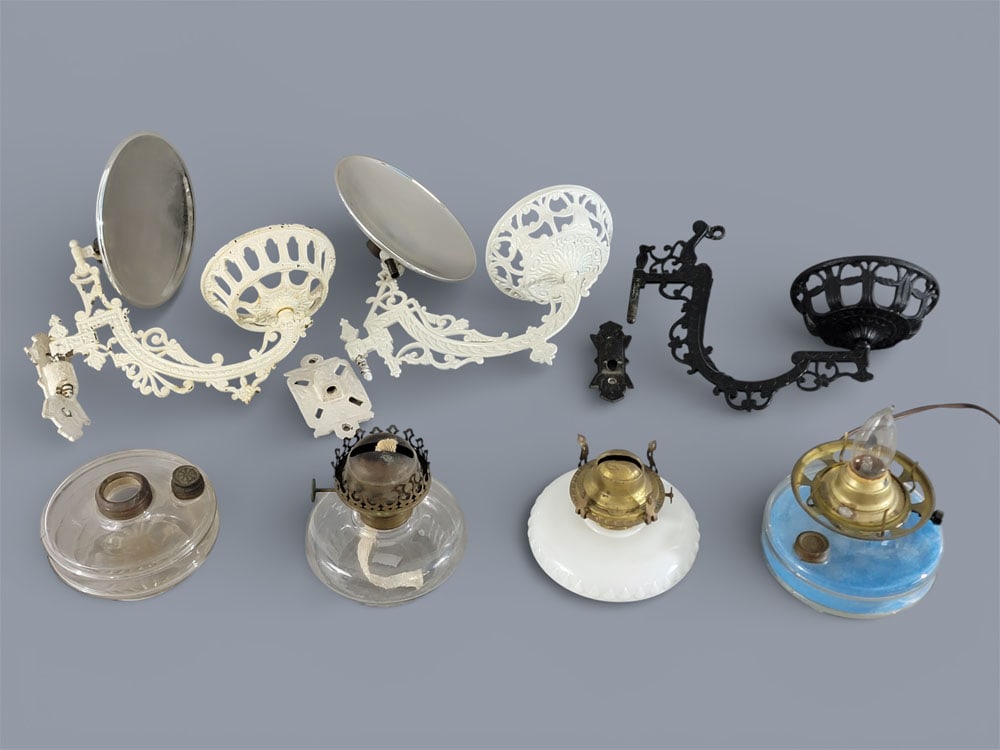 GROUP OF BRACKET LAMPS: American, 19th century, cast iron, brass, and glass. A group of kerosene bracket lamps, including three cast iron brackets with wall mounts, four glass and brass fonts, and two reflectors. Brackets 12