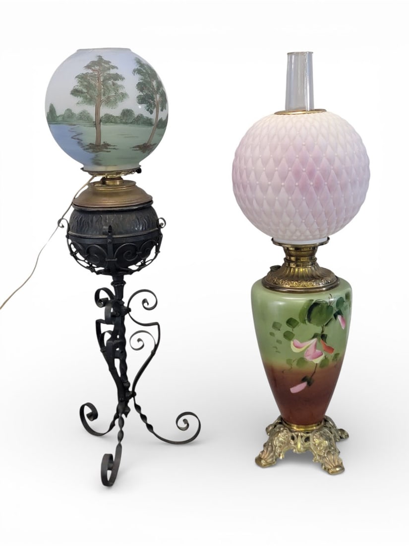 TWO BANQUET LAMPS: American, 19th century, cast iron, brass, and glass. Two electrified banquet lamps. A lamp with wrought iron column, cast iron font with flame design on shoulder, and painted glass globe featuring a t