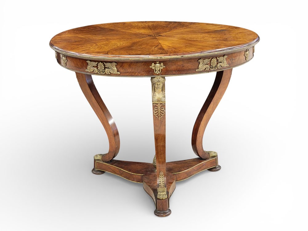 FRENCH EMPIRE-STYLE CENTER TABLE: Early 20th century. Round top with figured veneer and central inlaid star, the skirt and legs also with figured veneer and brass mounts, including faces and griffins. 32" high, 40" diameter. Provenanc