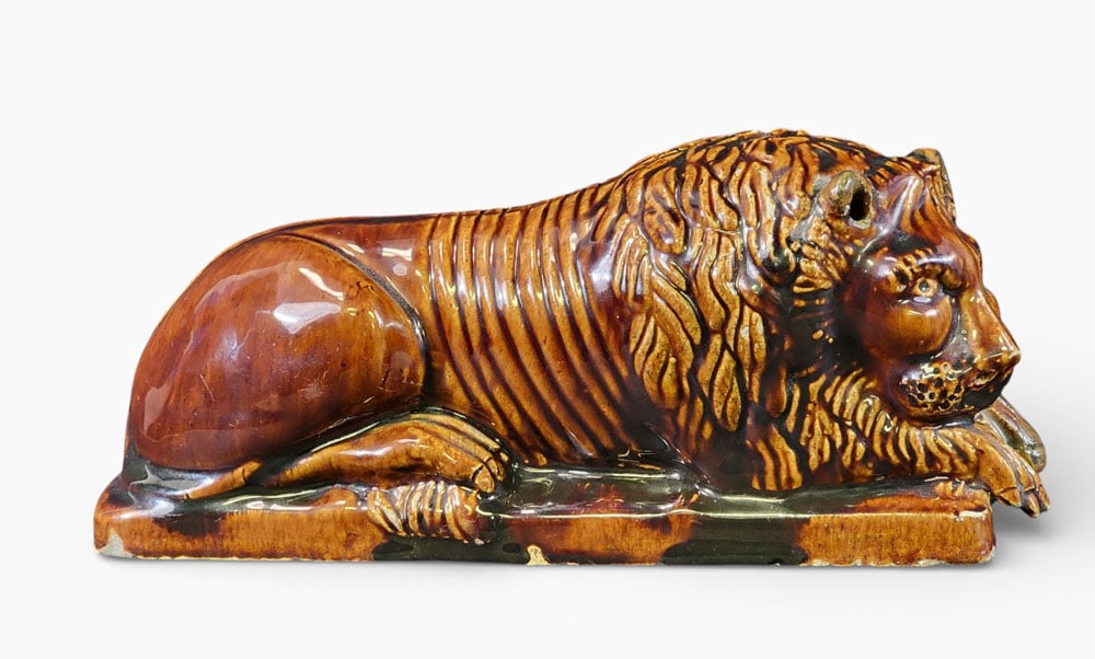HAIG POTTERY ROCKINGHAM LION: Faintly marked on the base "HAIG 1871" for James and Thomas Haig Jr., Philadelphia, Pennsylvania, and dated on the underside February 12. Nicely detailed recumbant lion with a Rockingham glaze. 9" lon