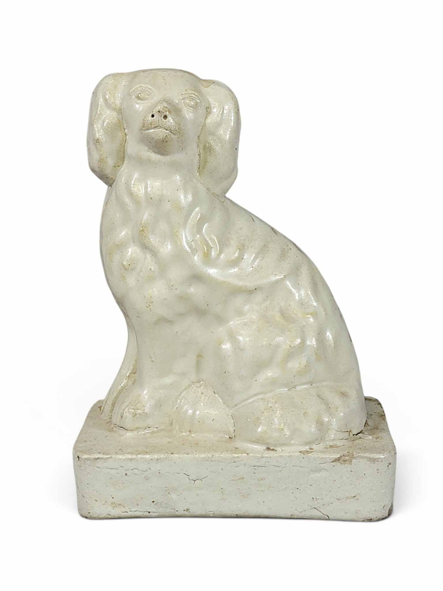 DIMINUTIVE STONEWARE DOG: Possibly Ohio, late 19th century. Small size, with a cream glaze. Both the dog and the base are molded and solid, and were bolted together prior to firing. 7" high. Provenance: an Ohio collection. NOT