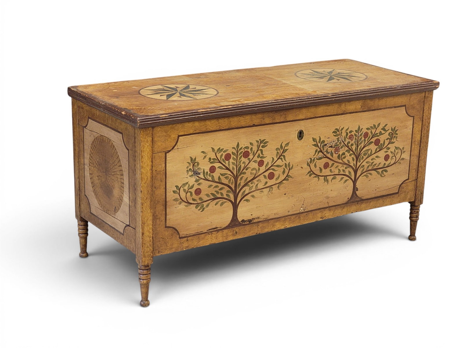 PAINT-DECORATED BLANKET CHEST: American, 1st half-19th century, pine. With turned legs, original strap hinges and bear trap lock, and with an older repaint consisting of apple trees and compass stars. 26" high, 51.25" wide, 21.5"