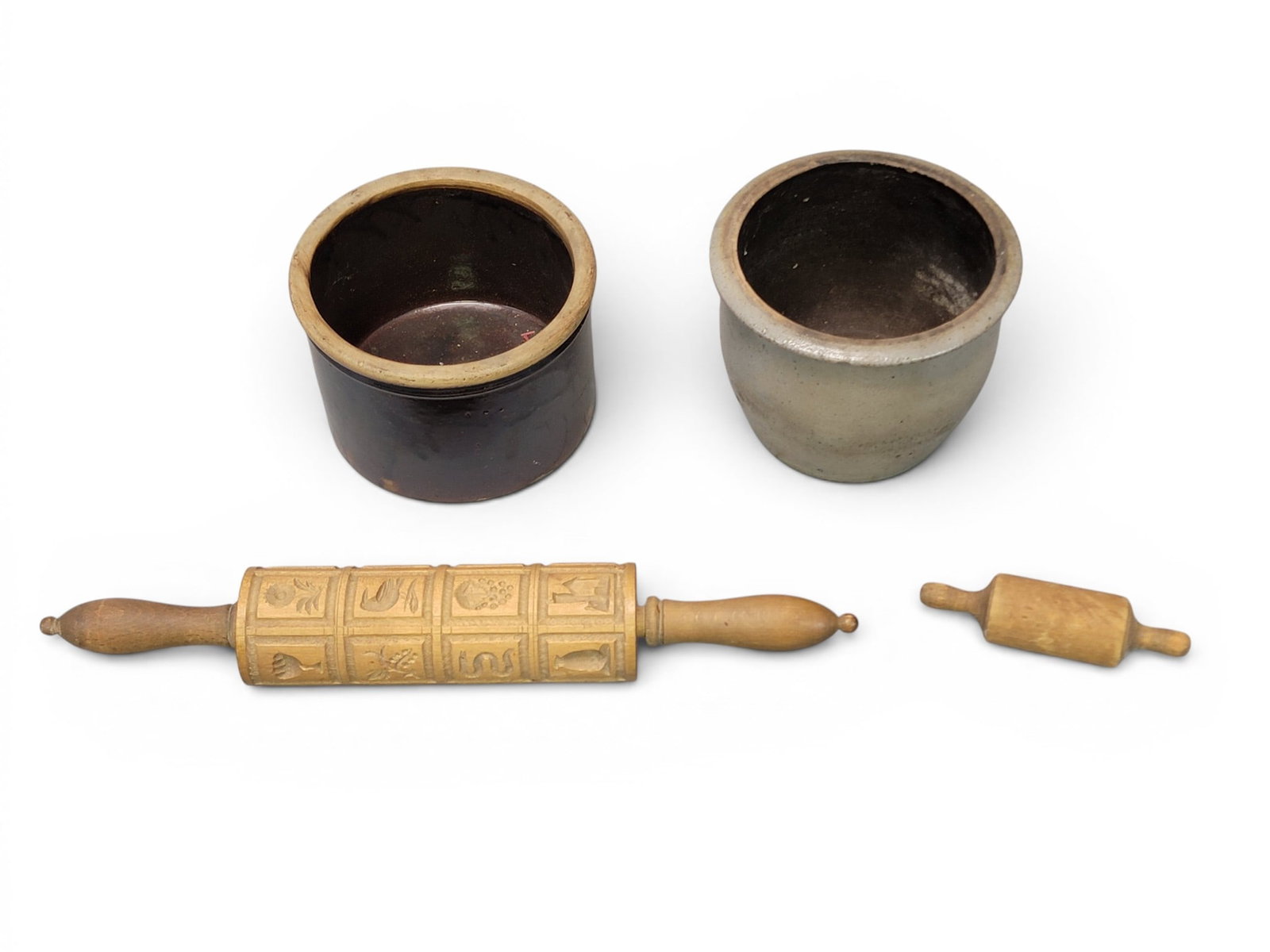 STONEWARE AND ROLLING PINS: American, 19th century. Includes a salt-glazed crock, 6" high, and an Albany slip-glazed crock, 5" high; together with a miniature rolling pin and a carved springerle rolling pint. 18" long.