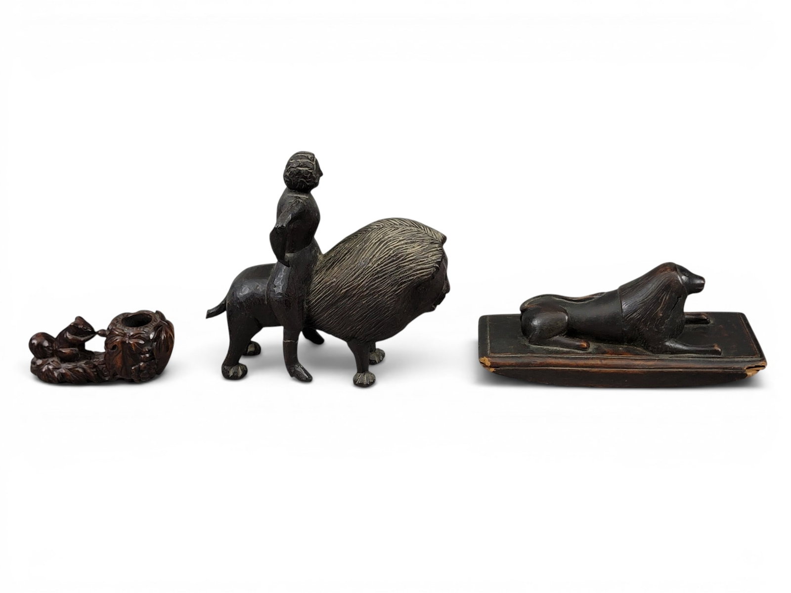 THREE FOLK ART CARVINGS: Late 19th-early 20th century. Includes a walnut blotter with recumbent lion, 9" long; together with a pipe bowl with squirrel, 5" long, and a stylized carving of a woman riding on the back of a