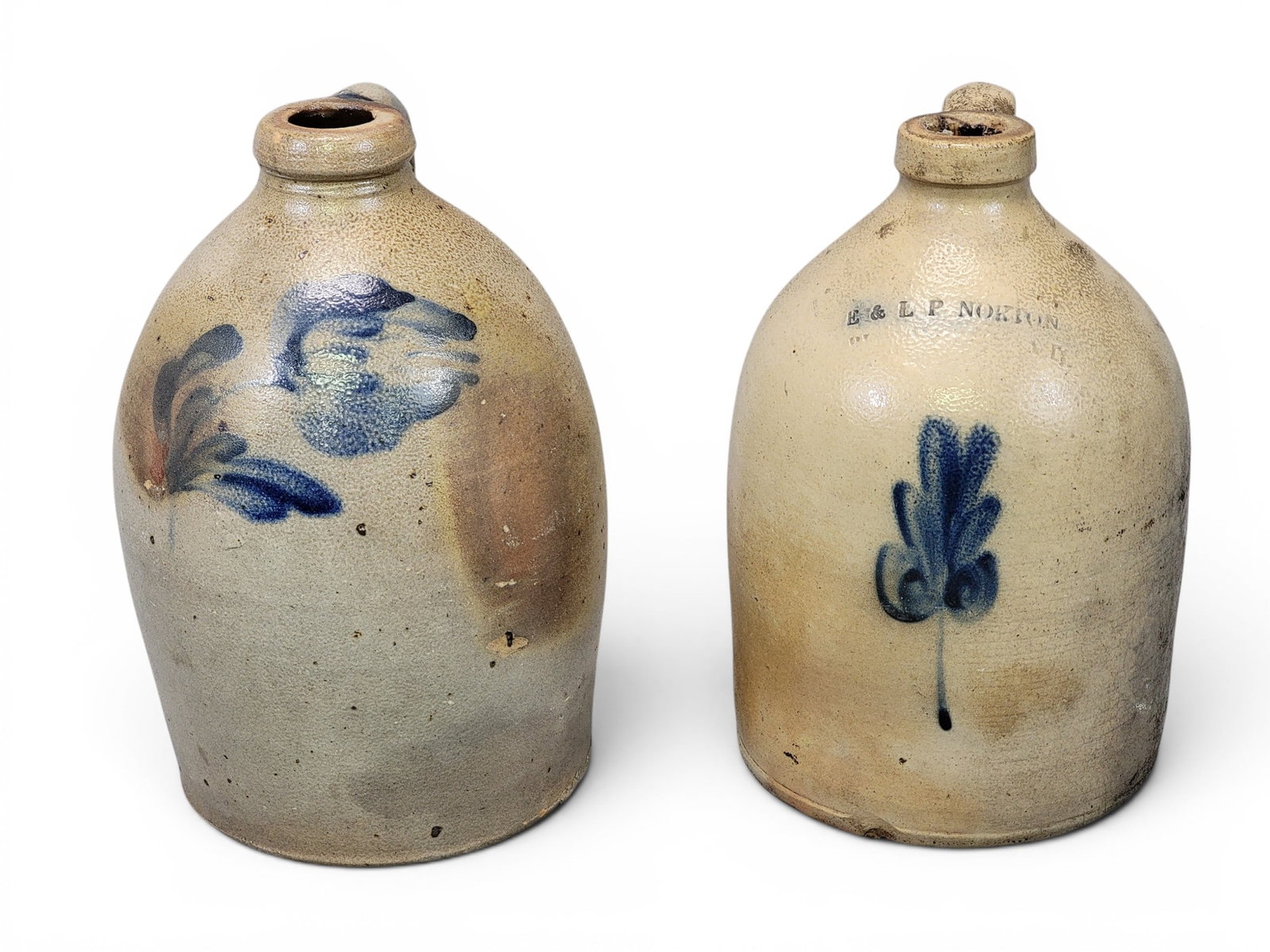 TWO DECORATED STONEWARE JUGS: Both approx. one gallon. Includes an E. & L.P. Norton jug with small leaf, 11" high; together with a jug with a cobalt tulip, 11" high. Provenance: a Pennsylvania collection. NOTE: We are happy to ans