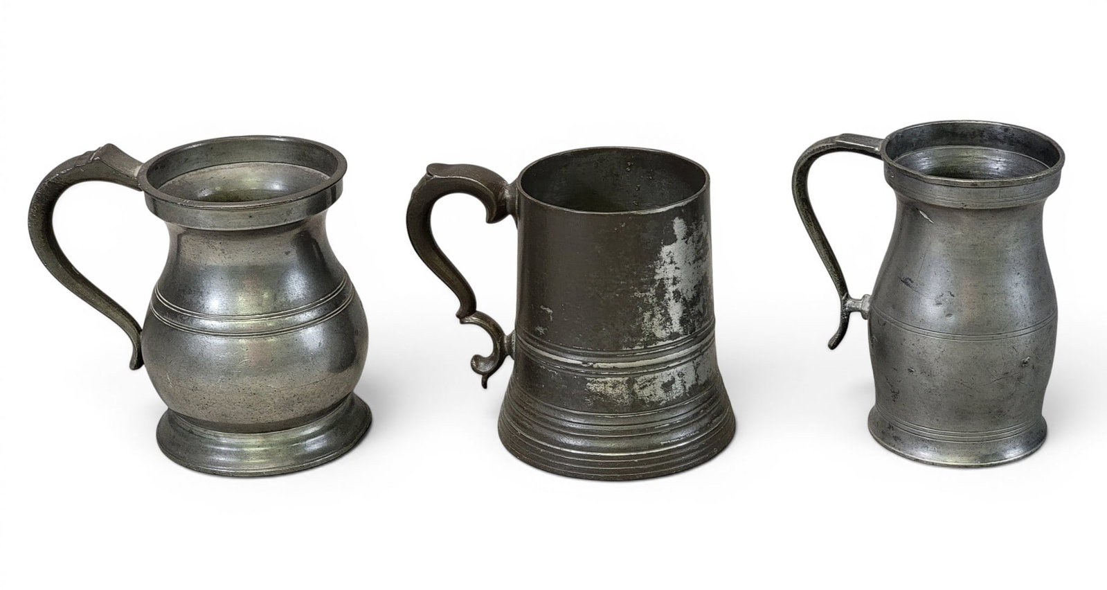 THREE PEWTER MUGS OR CANNS: Includes a bellied measure by Thomas Danforth and Company, New York, c. 1825, marked "TB&Co." and with "IPS" and "1825" stamped near the handle. 5.25" high; together with an unmarked English bellied
