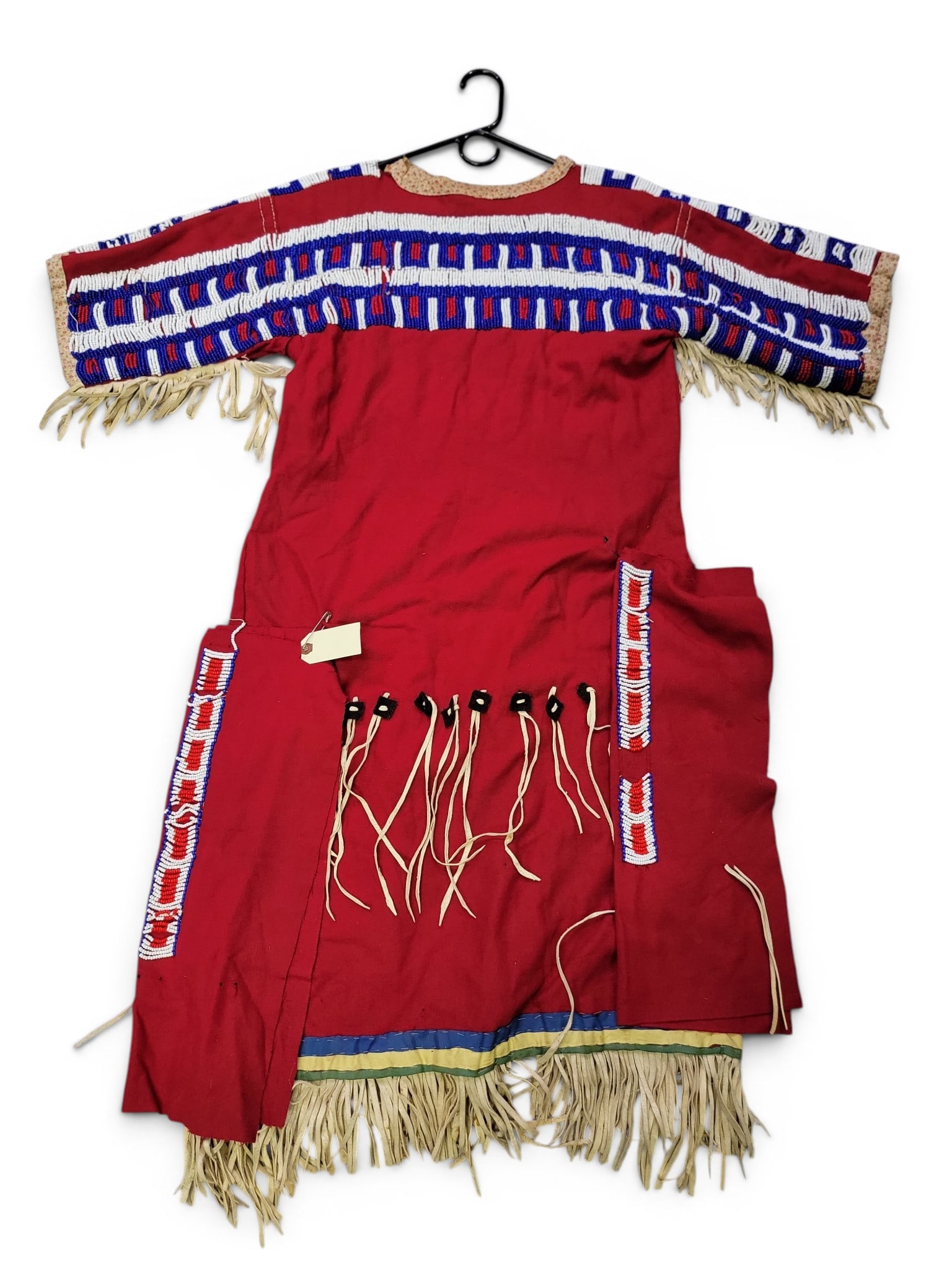 PLAINS-STYLE BEADWORK DRESS: Possibly Native American, mid-20th century. Red felt dress with printed fabric collar and sleeves, and silk ribbons at the lower hem, trimmed in leather fringe, and decorated with an estimated 30,000