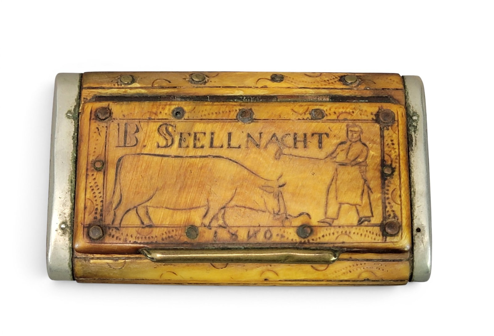 CARVED SNUFF BOX: Probably German, dated 1840. Flattened form with nickel silver and brass mounts. The front is carved with a man and cow, along with "B. SEELLNACHT" and dated 1840; the back is carved with a star and