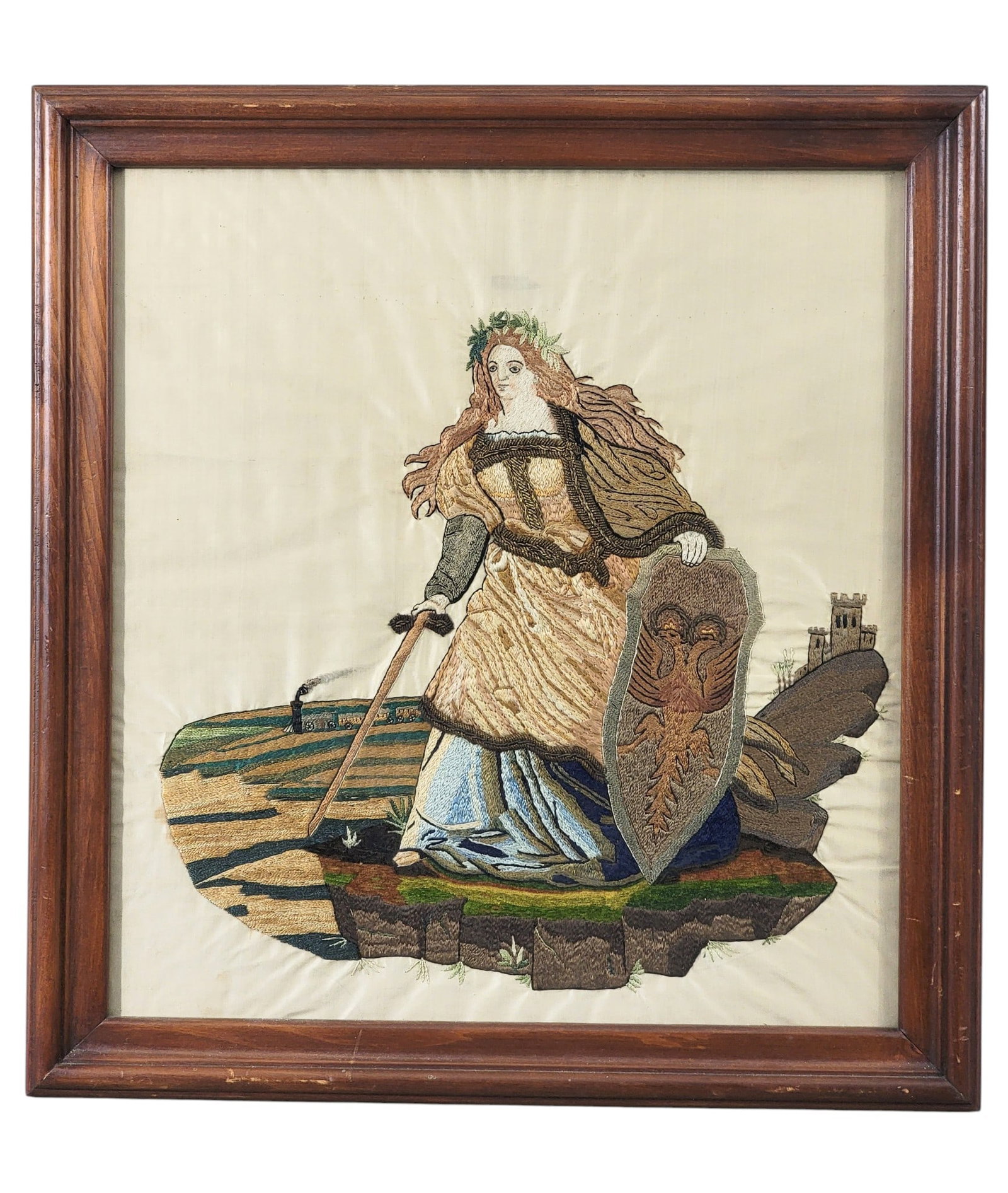 NEEDLEWORK PICTURE OF A WOMAN WARRIOR: European, 2nd half-19th century, silk and metallic thread on silk. Full-length portrait of a woman warrior with sword and shield, with a castle and a train in the background. In a later frame, 19.25"
