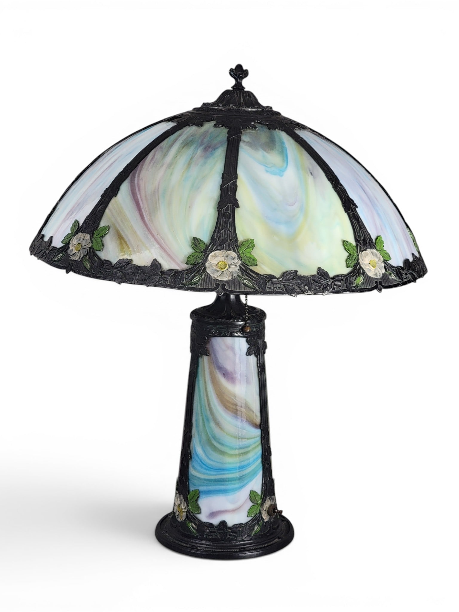 SLAG GLASS TABLE LAMP: American, 1920s. Both base and shade with cast and painted floral design, and both with panels of green, white, blue, and purple slag glass. 23" high; shade is 18.75" diameter. Provenance: a northeast