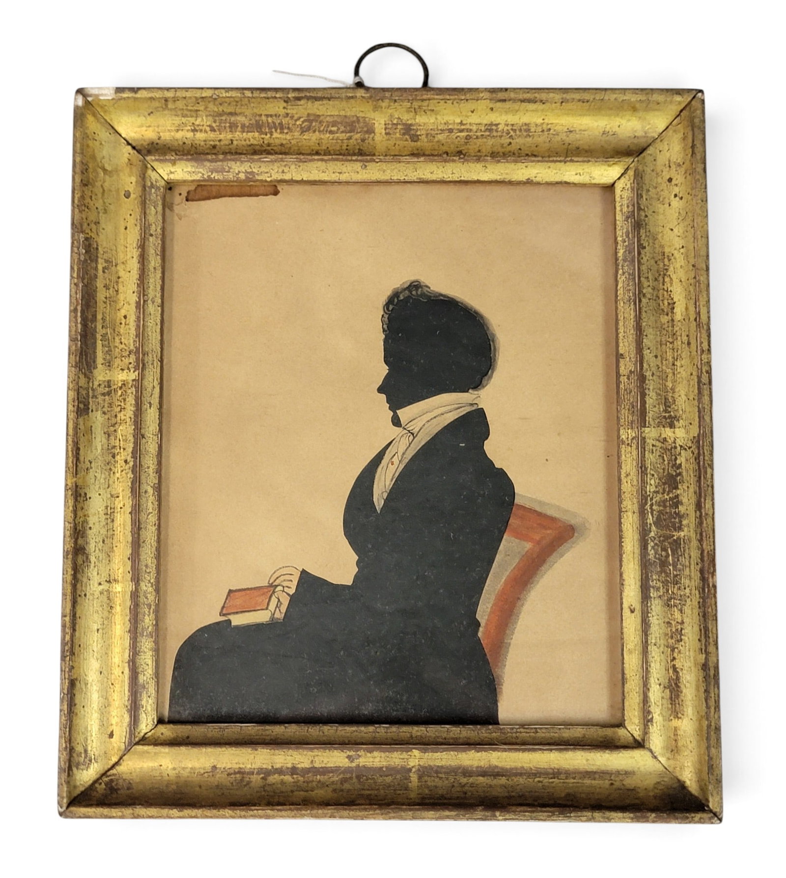 SILHOUETTE OF A GENTLEMAN HOLDING A BOOK: Possibly Philadelphia, Pennslyvania, dated 1828. Hollow-cut profile of a seated man, with ink and watercolor details, including a decorated chair and a red book. In its original frame that is dated