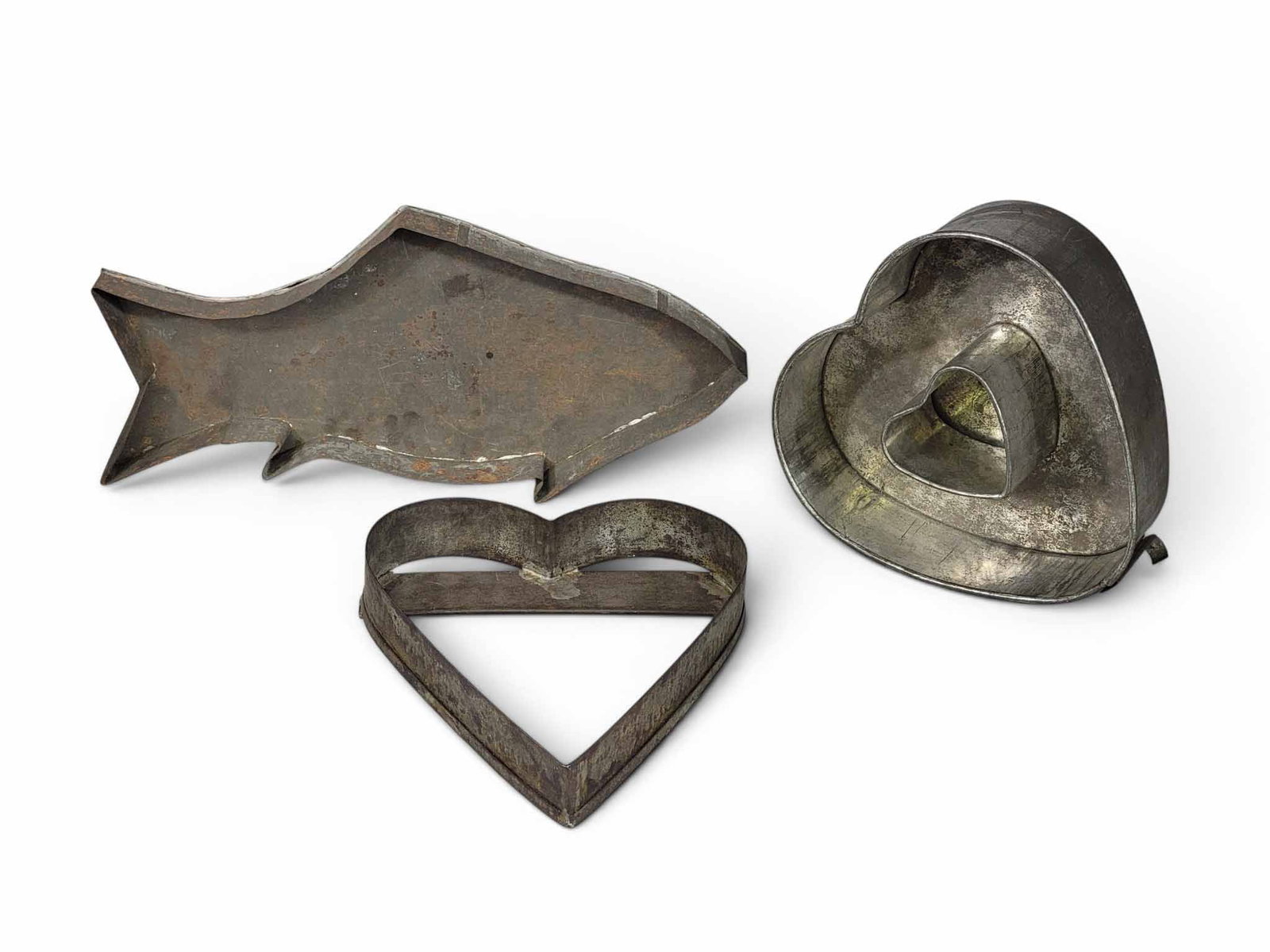 THREE TIN FOOD MOLDS: American, 19th century. Includes a large fish, 16.5" long; together with two hearts (one of which is a cake pan, 11" and 9" long. Provenance: a New York State collection NOTE: We are happy to answer