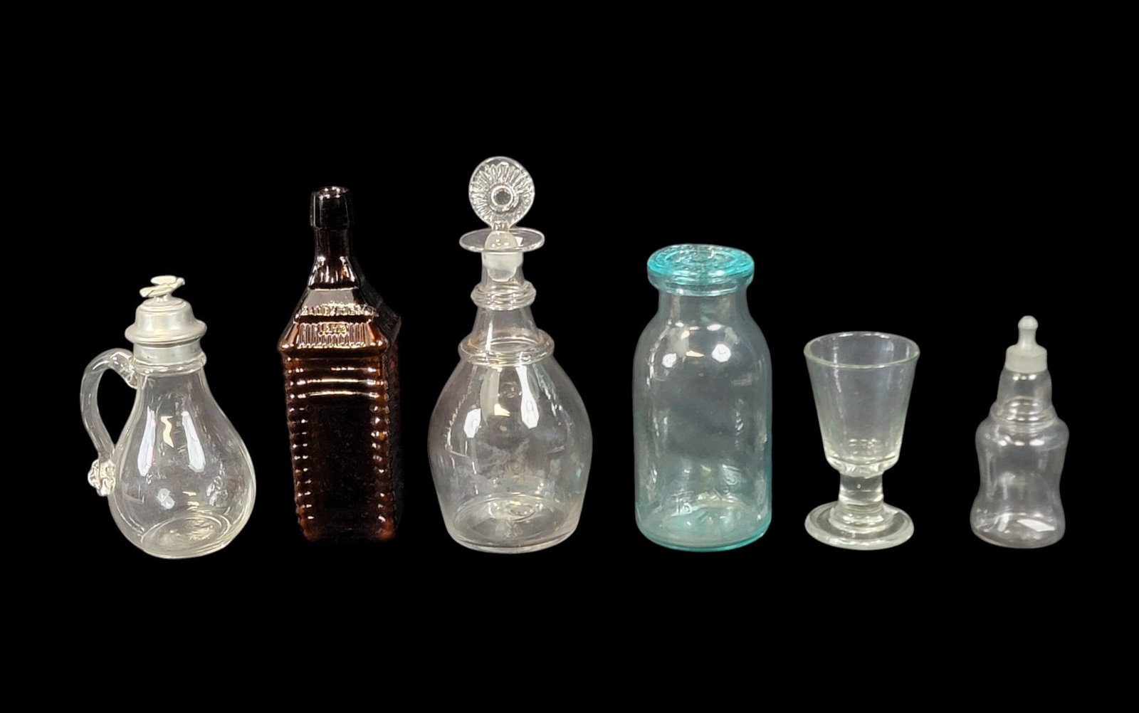 COLLECTION OF GLASS BOTTLES AND WARES: American, 19th century. Includes an amber Drake's Bitter's log cabin bottle, 10.25" high; a Whitall's Patent fruit jar with lid, 8.25" high; a blown decanter with applied rings, 11" high; a nursing bo
