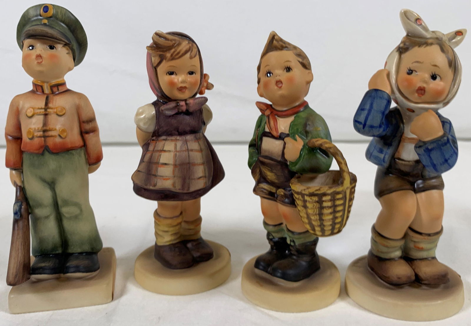 Lot of Four Goebel Hummel Figurines: Vintage lot of 4 goebel hummel figurines. 1) "Soldier Boy" depicting a young soldier boy dressed in uniform holding a firearm. 6in H x 2in L. 2) "Boy w/ Toothache" depicting a young boy with a tooth a