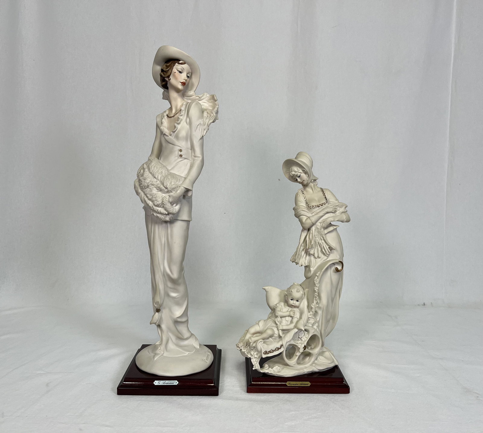 Giuseppe Armani Porcelain Figurine Pair: Pair of Giuseppe Armani Porcelain Decorative Figurines including "Lady with Muff" a young tall and slender groomed lady holding a fur muff striking a pose 18.75" H x 5.5" W x 5.25" L and "Mother Child