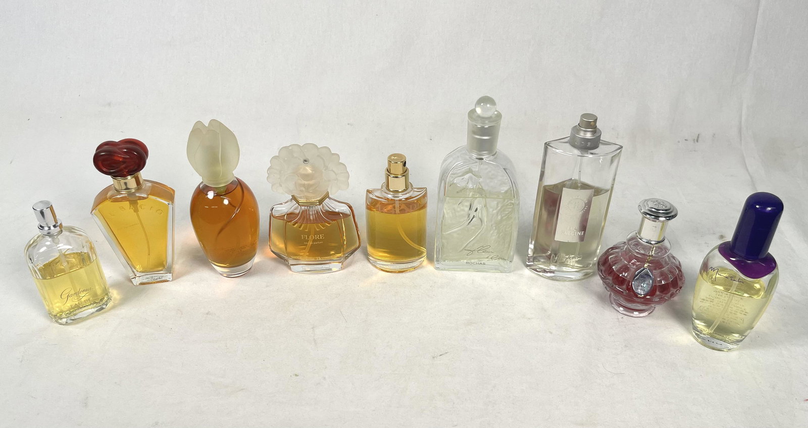 Lot of 9 Perfumes: Lot of 7 Perfume Bottle 1x Murasaki 1.7 FL OZ 1x Rochas Fleur D'eau 3.4 FL OZ 1x Carolina Herrera Flore 1.7 FL OZ 1x Gardenia 1.7 FL OZ 1x Suggestion Eau D'argent Claude Montana 3.4" FL OZ 1x Joop Per