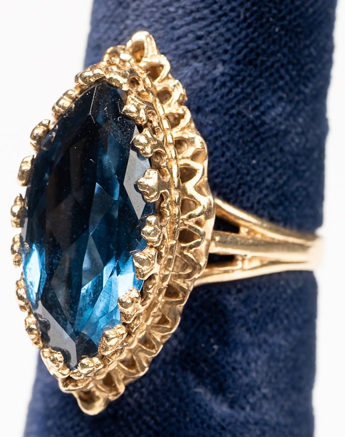 14K Gold Blue Stone Cocktail Ring: 14Kt Yellow Gold Blue Stone Cocktail Ring Featuring a Partially Split ShankLarge Marquise Cut Blue Stone in Deep Oceanic Blue Color in Multi Prong Ornate Setting Halo which Gives it an Art Deco Mid Ce
