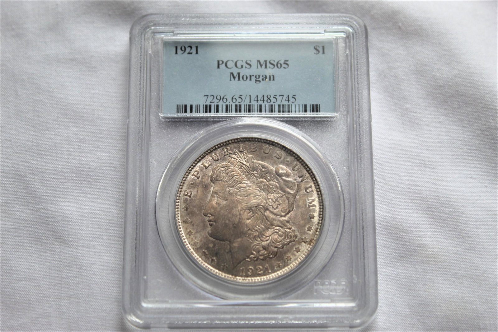 Graded 1921 MS65 Morgan Dollar: This 1921 $1 Dollar Coin is graded by PCGS as 1921 MS65 Morgan $1 Coin. It is designed by George T Morgan and is composed of silver 0.9000 measuring 38.1mm in diameter and weighing 26.7300g. As always