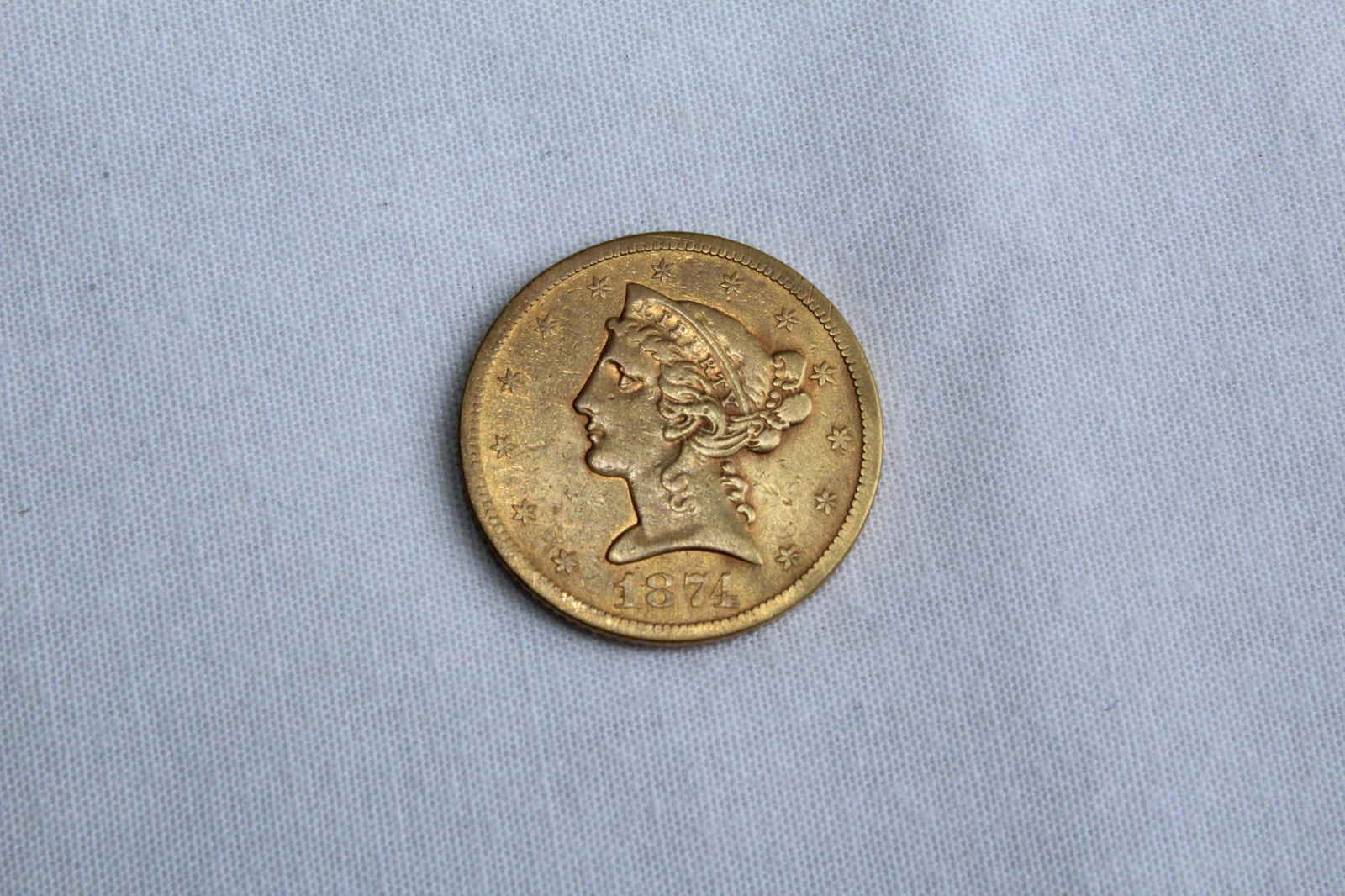 Liberty Head $5 1874 Gold Coin: This antique Five Dollar Liberty Head Coin features a left facing Lady Liberty profile on the obverse with 13 stars circling the coin and the year of the minting on the bottom. On the reverse it has a