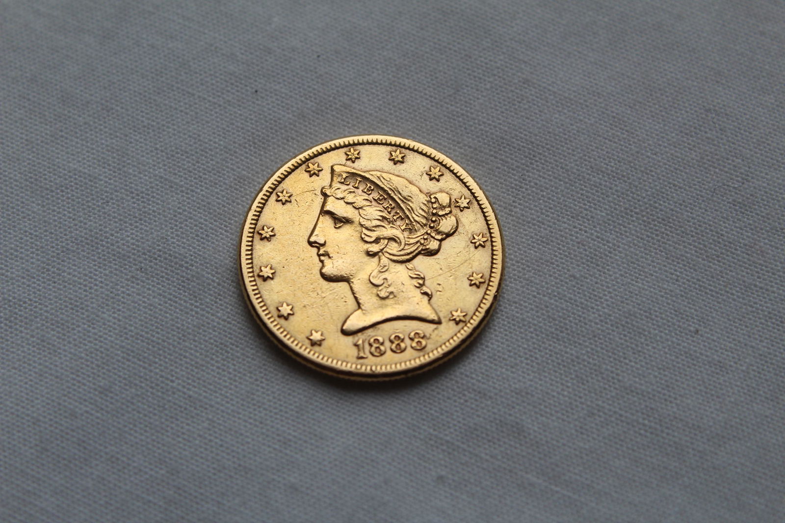 Liberty Head $5 1888-S Gold Coin: This antique Five Dollar Liberty Head Coin features a left facing Lady Liberty profile on the obverse with 13 stars circling the coin and the year of the minting on the bottom. On the reverse it has a