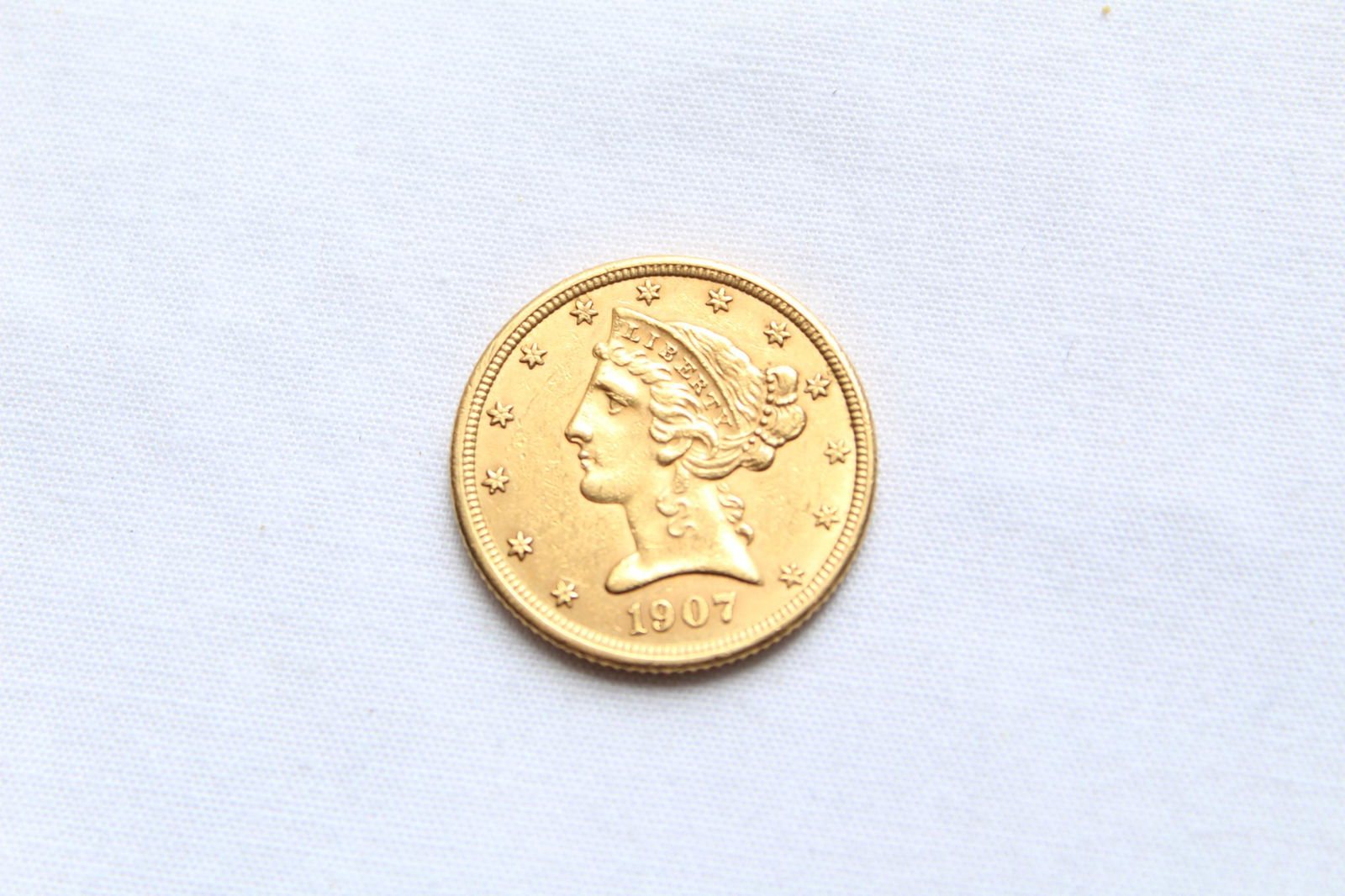 Liberty Head $5 1907 Gold Coin: This antique Five Dollar Liberty Head Coin features a left facing Lady Liberty profile on the obverse with 13 stars circling the coin and the year of the minting on the bottom. On the reverse it has a