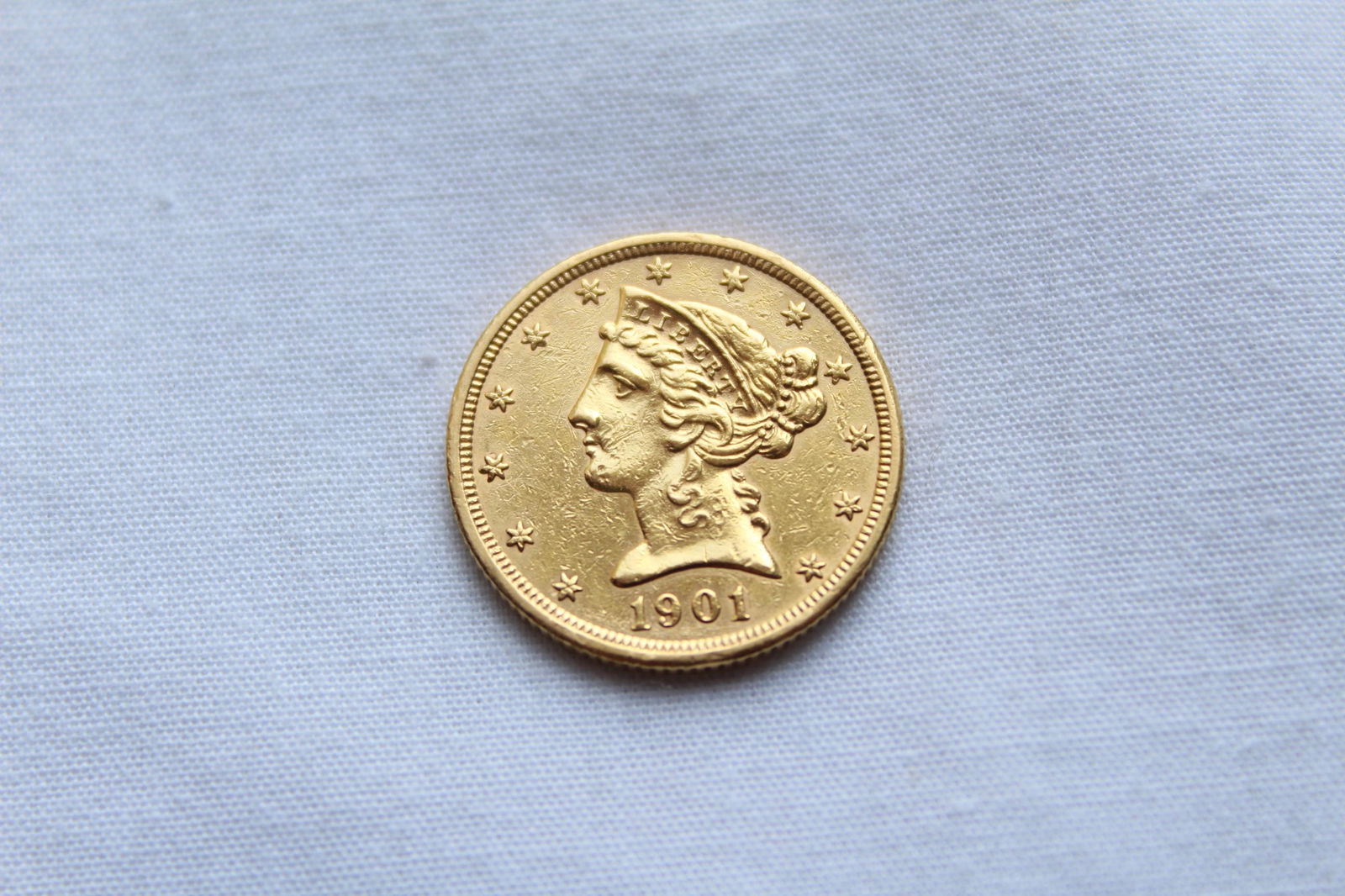 Liberty Head $5 1901 Gold Coin: This antique Five Dollar Liberty Head Coin features a left facing Lady Liberty profile on the obverse with 13 stars circling the coin and the year of the minting on the bottom. On the reverse it has a