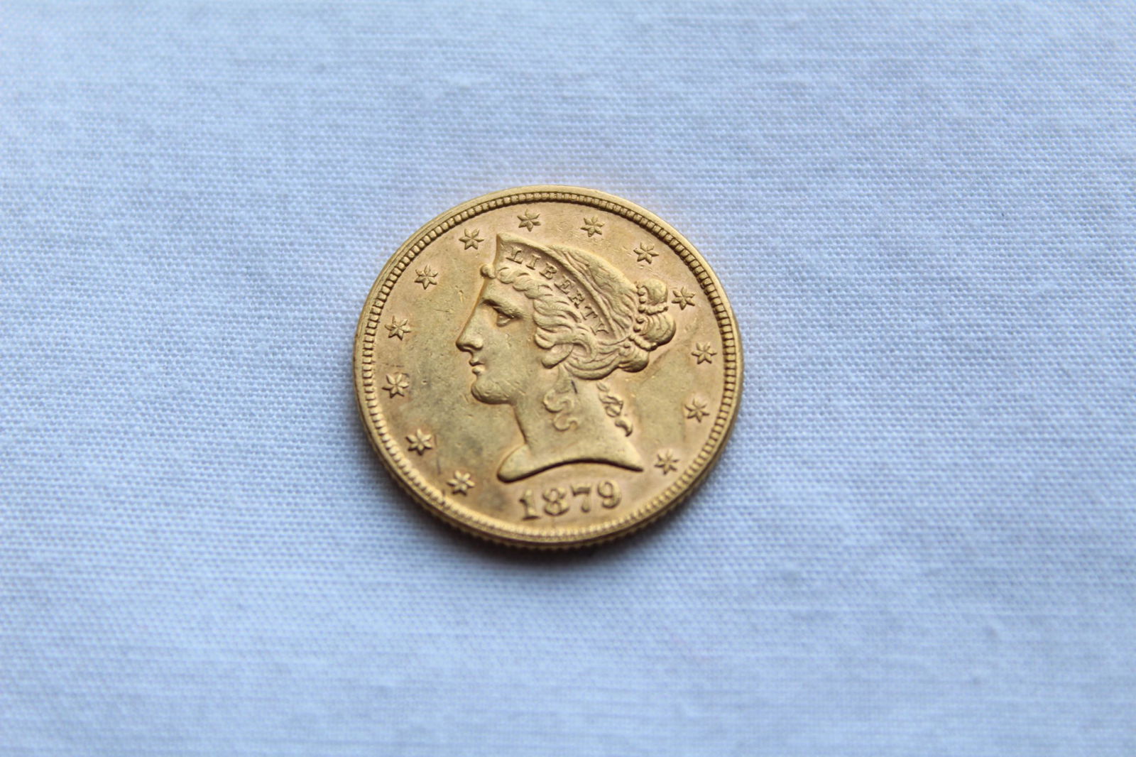 Liberty Head $5 1879 Gold Coin: This antique Five Dollar Liberty Head Coin features a left facing Lady Liberty profile on the obverse with 13 stars circling the coin and the year of the minting on the bottom. On the reverse it has a