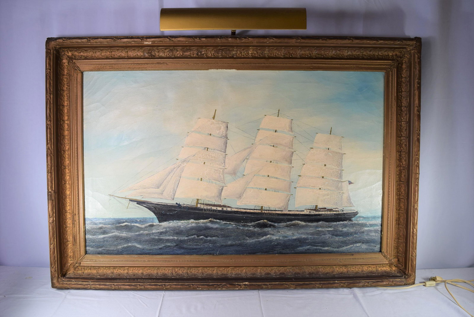 Large Gold Framed Oil On Canvas Of Ship: This beautiful ships painting sits inside a gold frame with artist light attached. This ships painting has craquelure all around and could use a cleaning otherwise in good overall condition. The frame