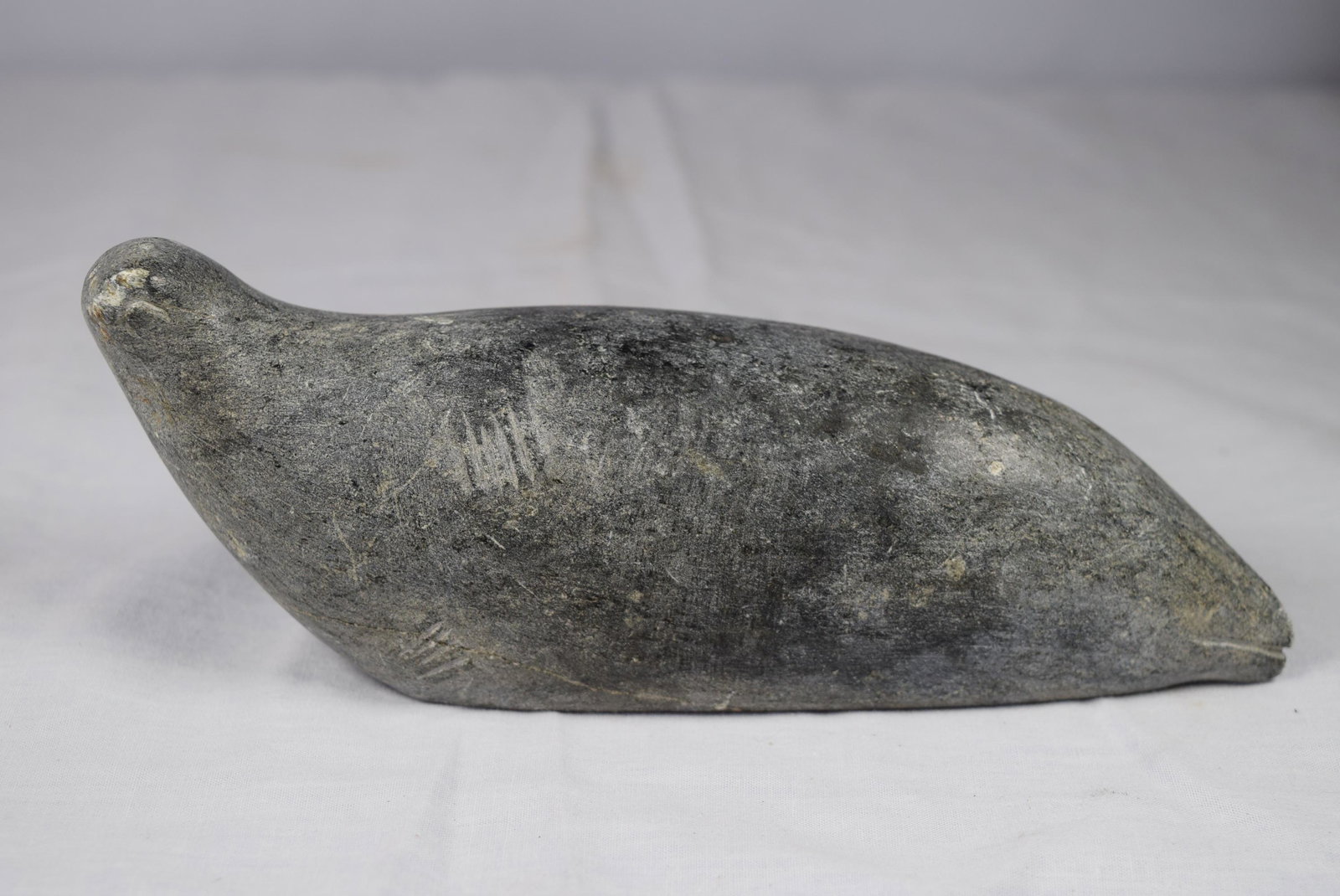 Inuit Carving of Seal: This Inuit carving features a seal laying down. This is singed on bottom TONGO E9-124. Measures 7in L overall. Made of soapstone. Some handling ware such as scratches otherwise appears in great condit