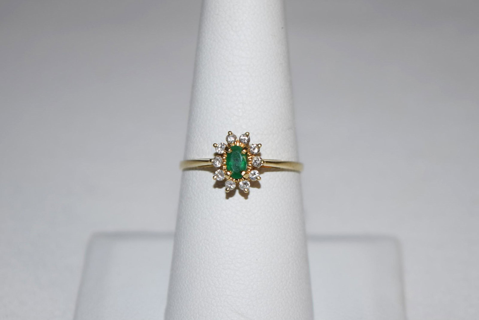 14K Yellow Gold Emerald Ladies Ring: Beautiful 14K Yellow Gold Emerald Ladies Ring features a round cut emerald in the center encircled by a halo of round cut diamonds in a floral-like design. This beautiful ladies ring currently measure