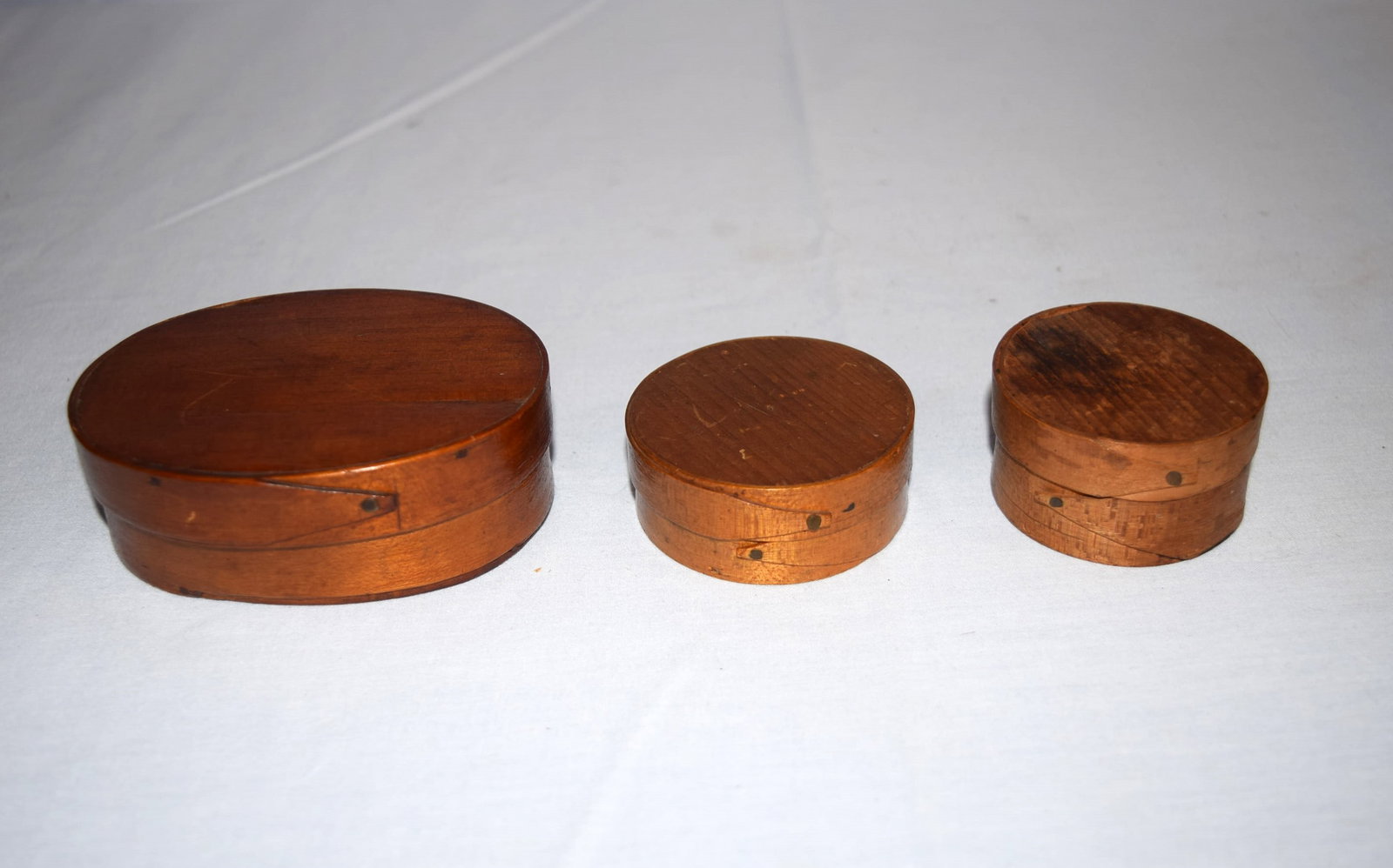 Lot of Three Shaker Wooden Boxes: Lot of Three 2-Finger Shaker Wooden Boxes measuring from largest to smallest: 4 inches long X 3 inches wide X 1.5 inches tall, nearly 2.5 inches round X 1 inch tall, and nearly 2 inches round X 1.25 i