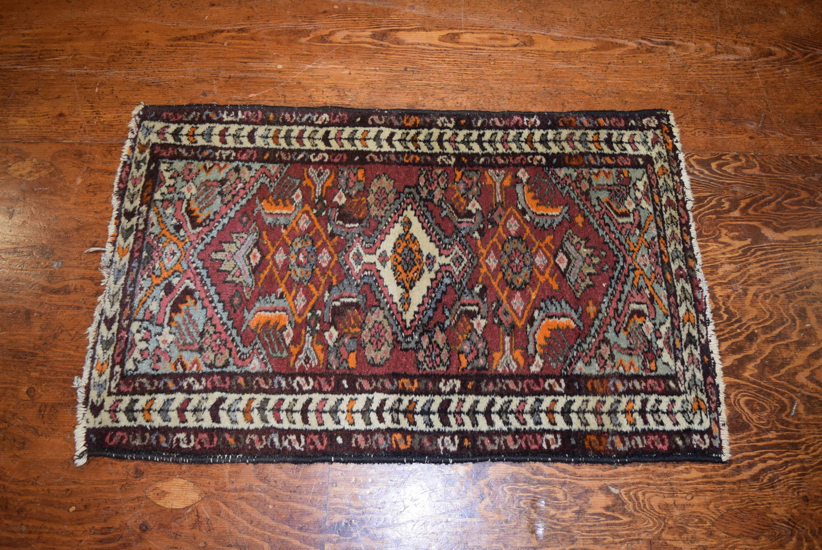 Small Antique Oriental Throw Rug: Small Antique Oriental Rug. Made in Iran. Tags still intact. Wear and damage due to age as seen in photos. Features muted reds, orange, pinks and light blue. Would add charm to any home, office or sho