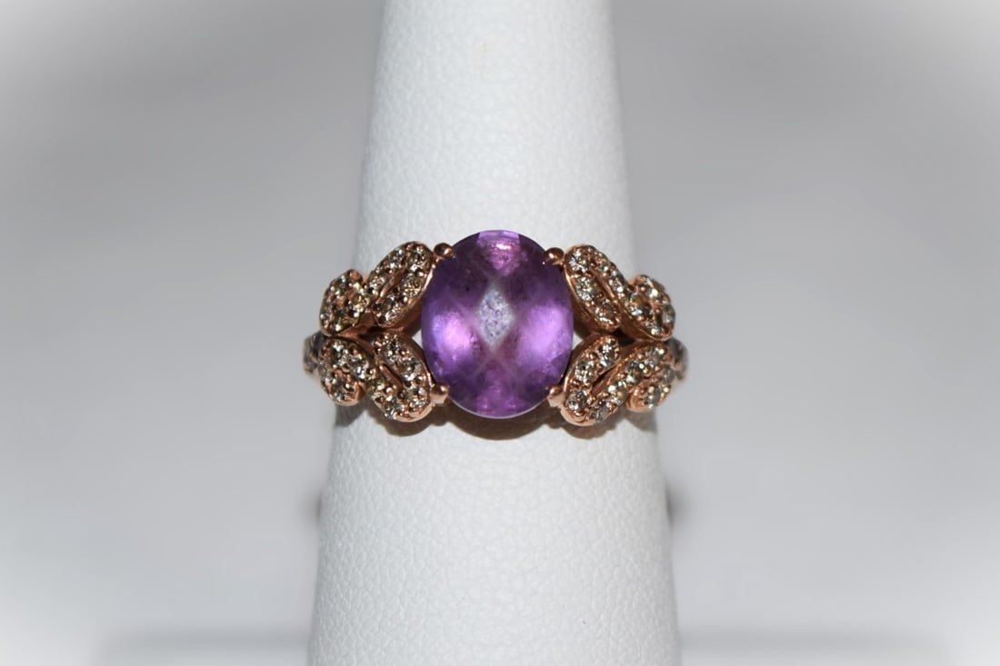14K Yellow Gold Purple Stone Ladies Ring: 14K Yellow Gold Purple Stone Ladies Ring. Features a large oval cut purple stone in the center believed to be an amethyst based on color and karat of band. Band has a floral-style wrap design adorned 
