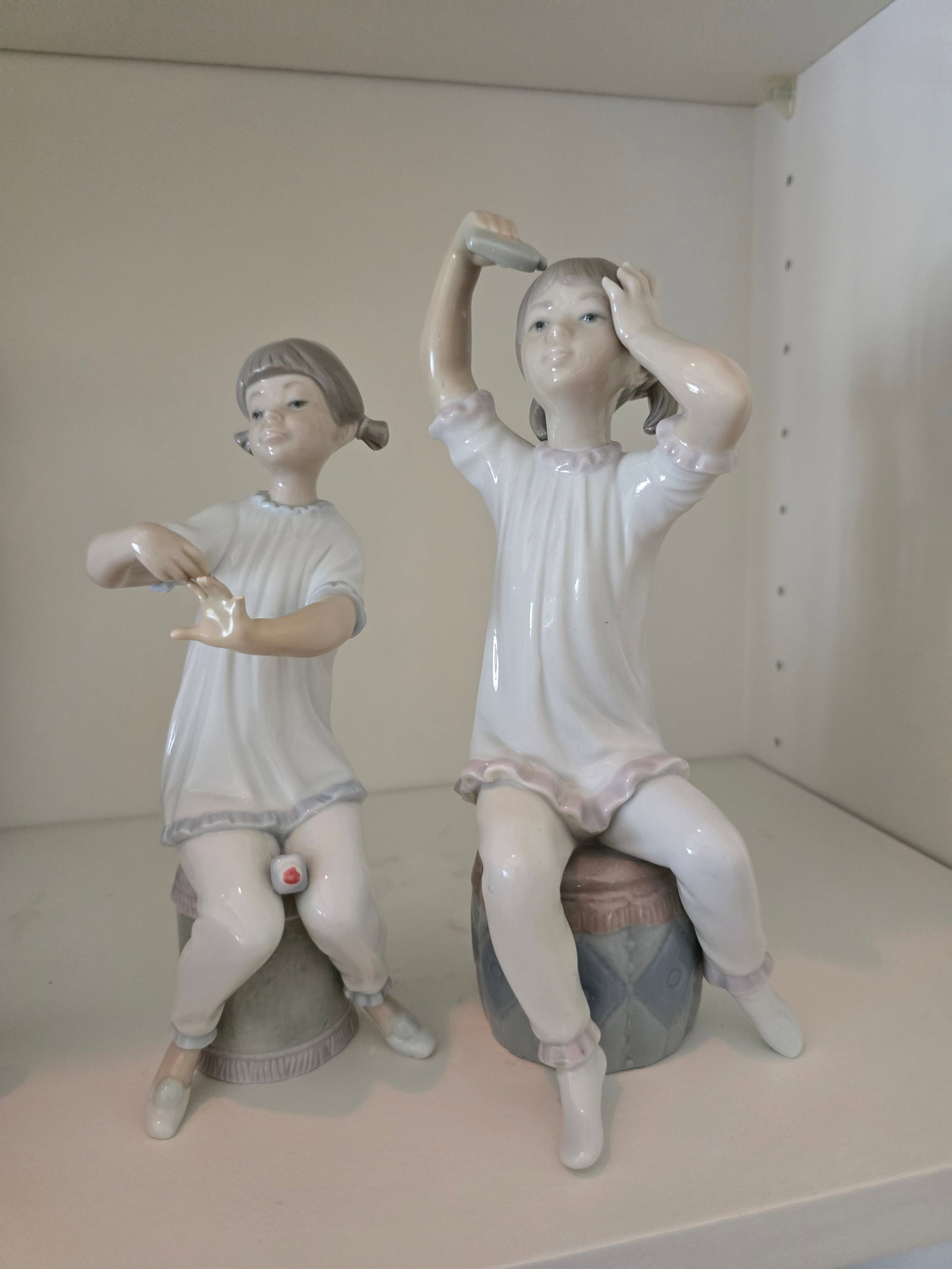 Two Lladró Porcelain Seated Girl Figurines: ITEM DESCRIPTION Group of two Lladró glazed porcelain figurines depicting young girls seated at their toilette, including a girl combing her hair and a smaller seated girl. Offered together as one lo