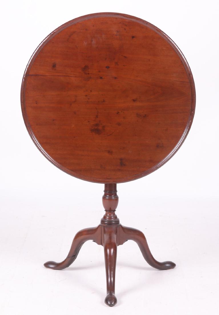 English Mahogany Queen Anne Tea Table: 18th century. Tripod base with snake feet, cabriole leg, below the urn turned shaft and birdcage, all below the tilting and rotating dished top. Dimensions: The top is 26 1/4" with the grain, 25 5/8" 